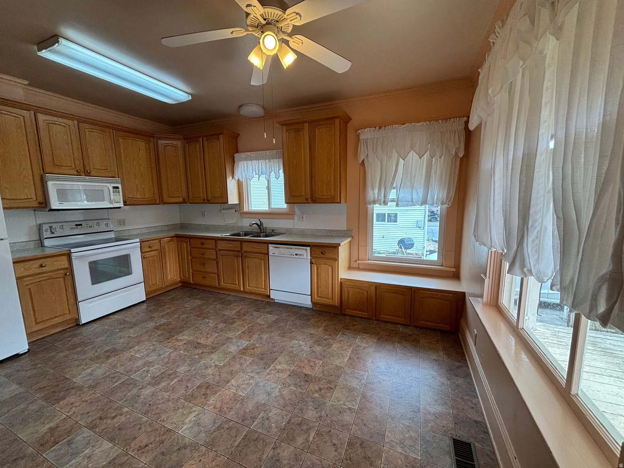 Kitchen featuring white appliances, stone finish floors, a ceiling fan, light countertops, and crown molding