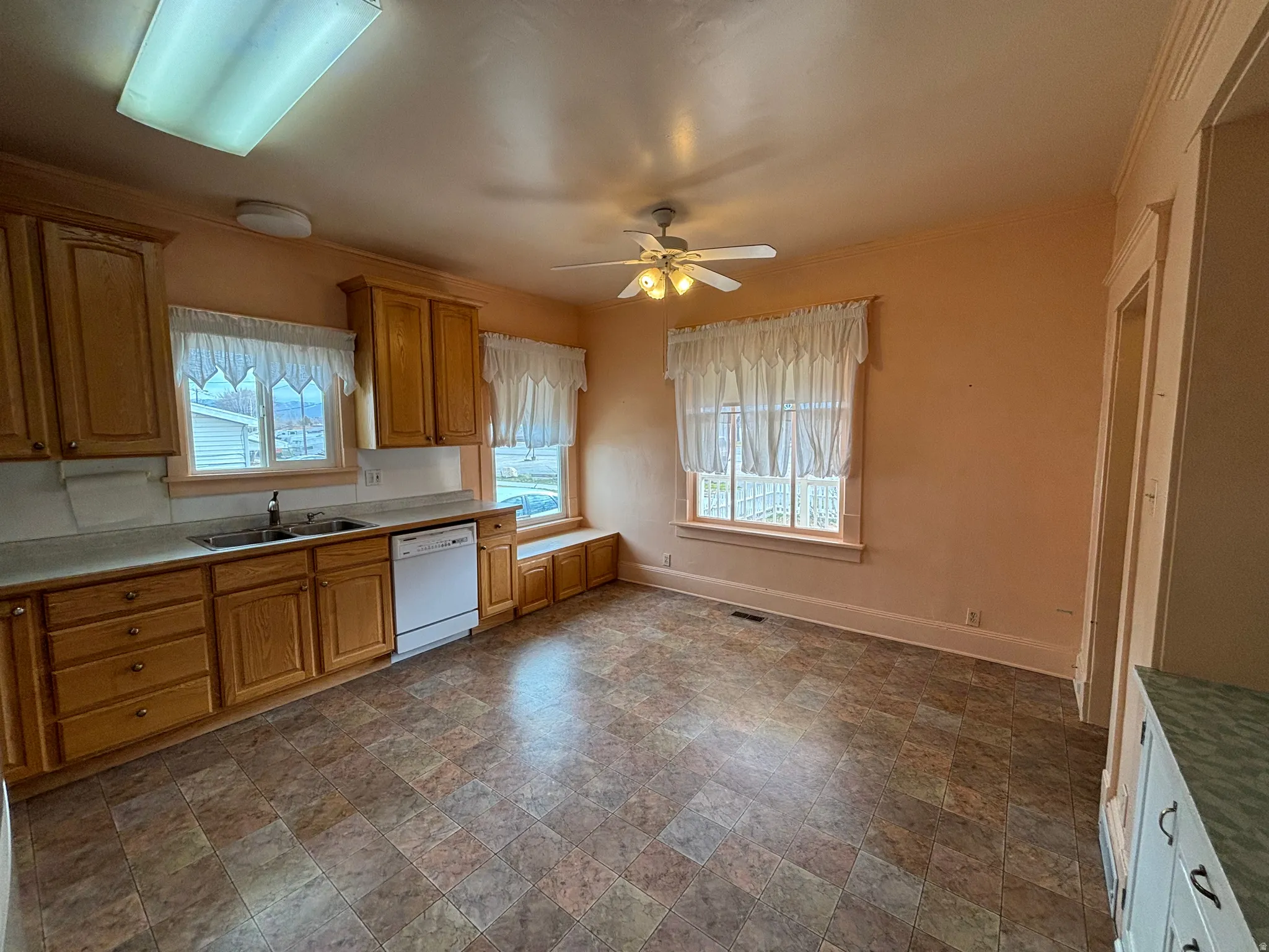 Kitchen featuring stone finish floors, ceiling fan, light countertops, white dishwasher, and crown molding