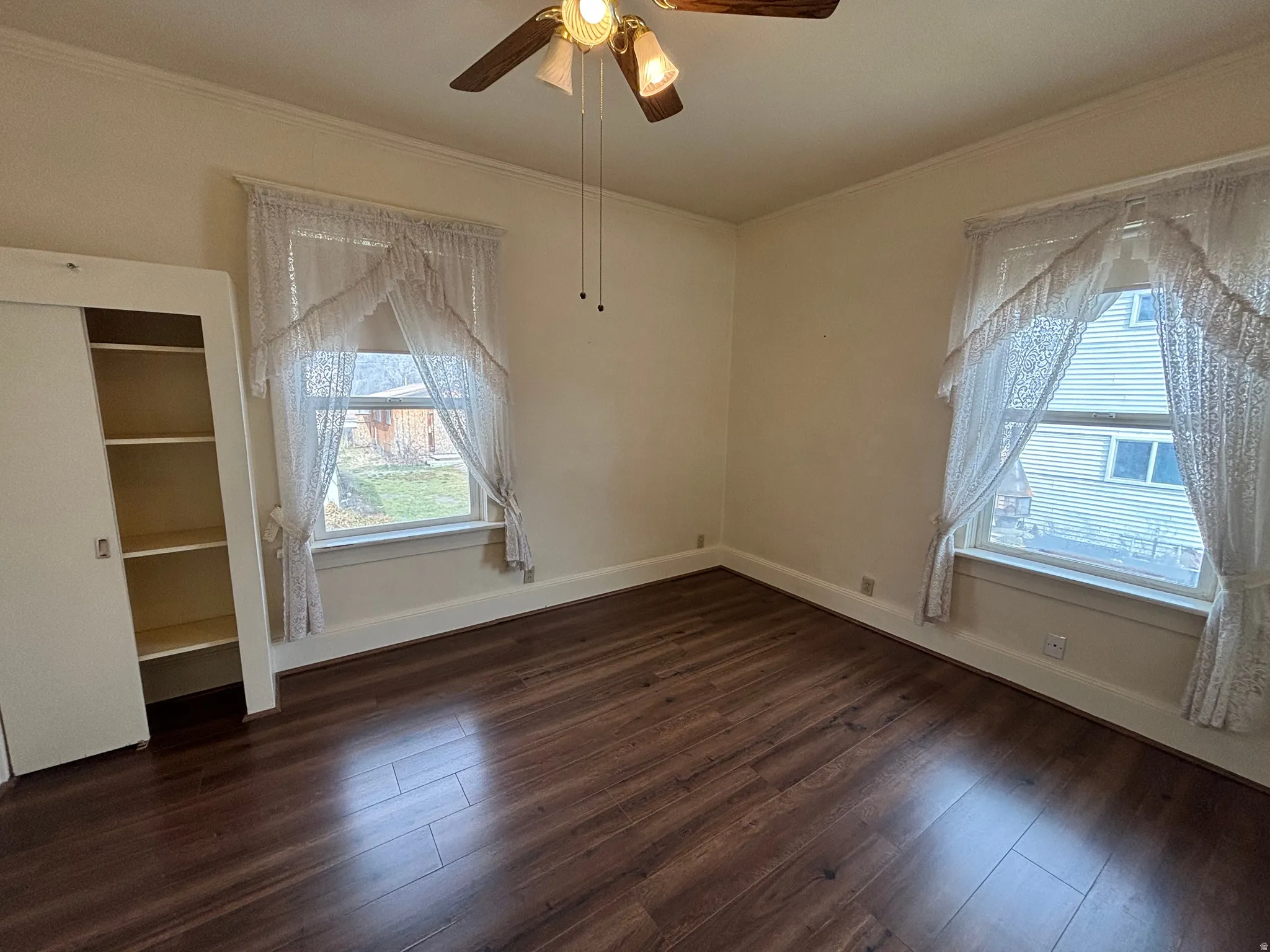 Empty room with dark wood-style flooring, a ceiling fan, and crown molding