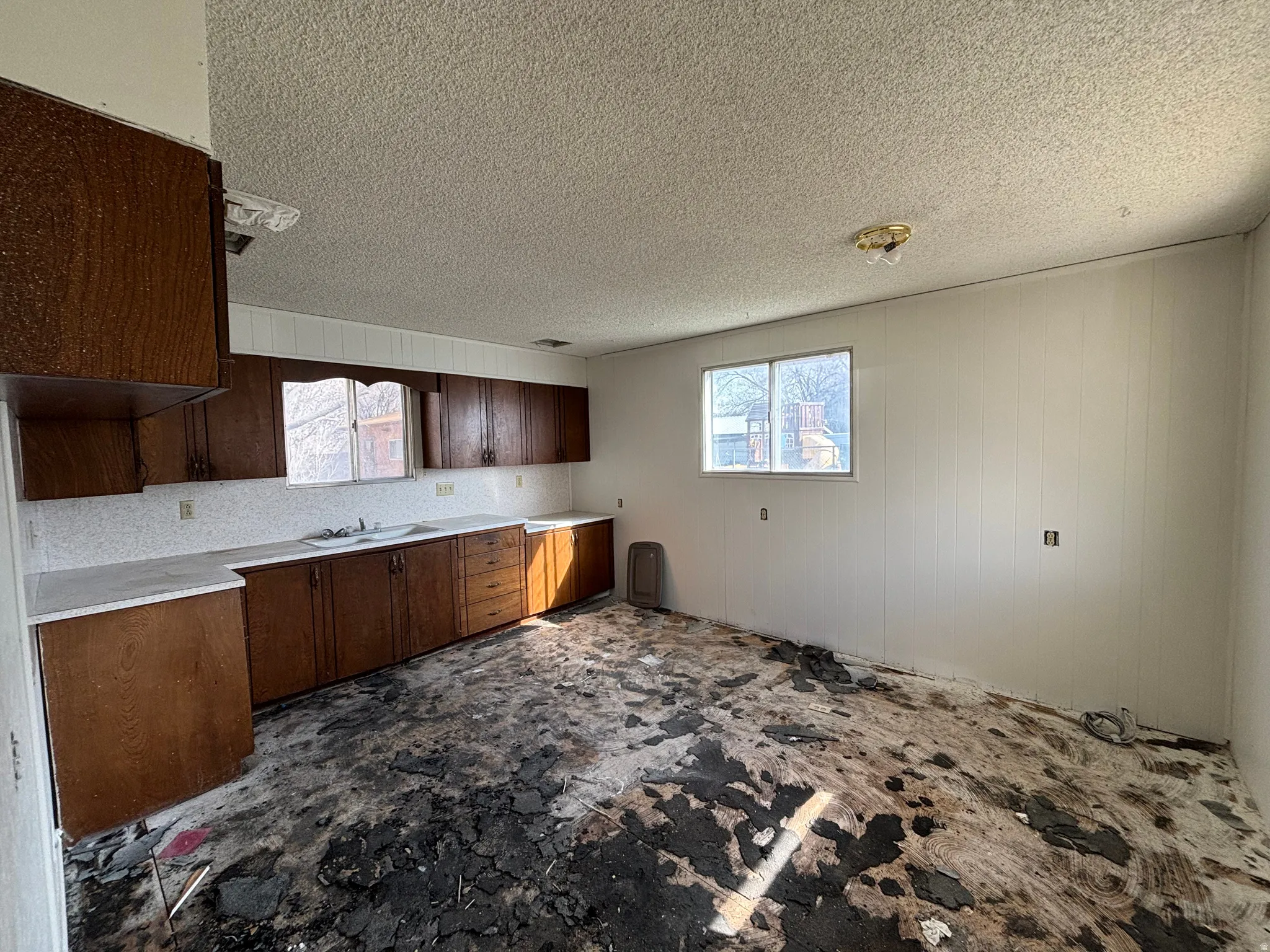 Kitchen featuring dark wood finish cabinetry, light countertops, a textured ceiling, and wooden walls