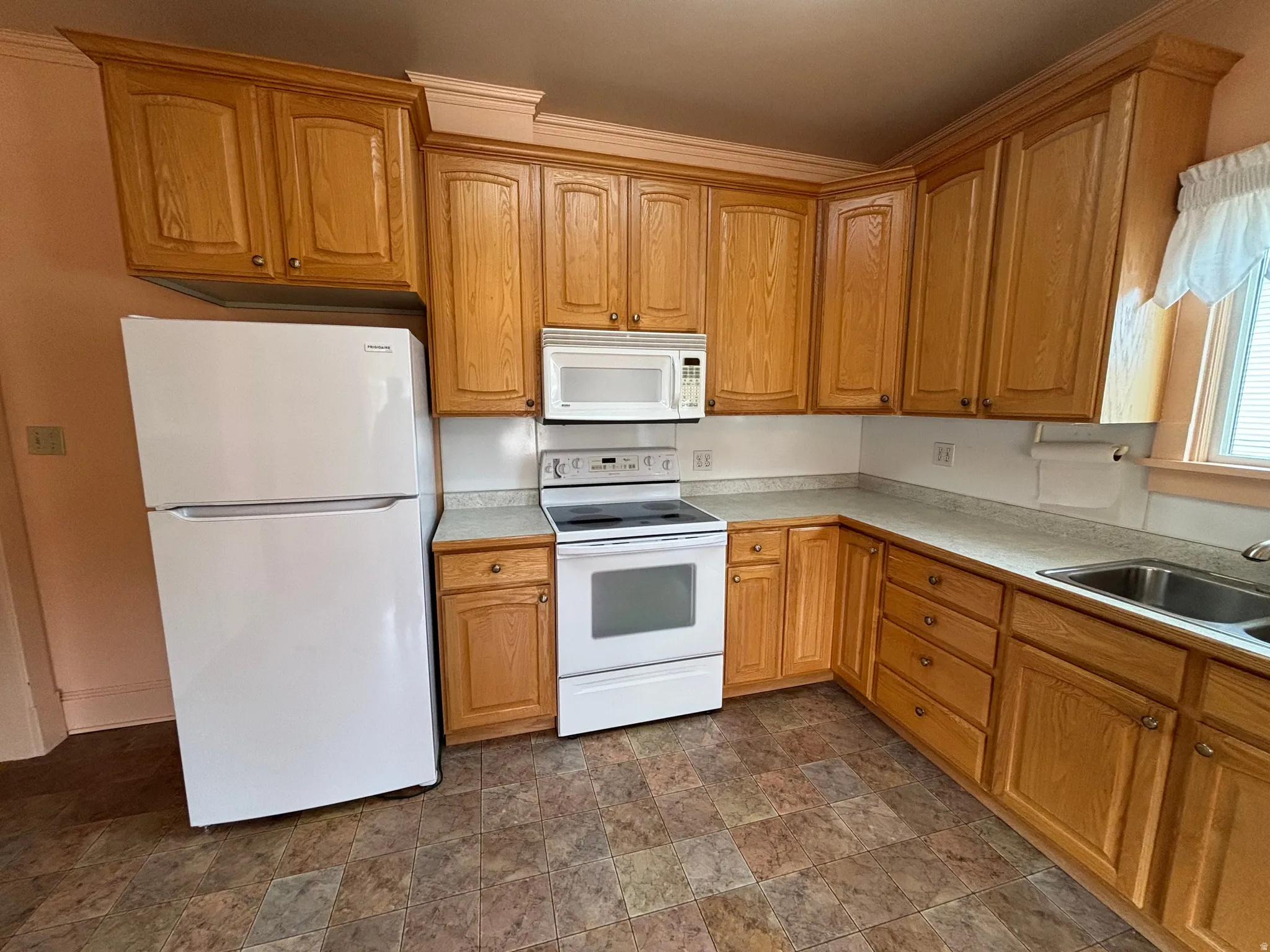 Kitchen featuring white appliances, stone finish flooring, light countertops, and wood finish cabinetry