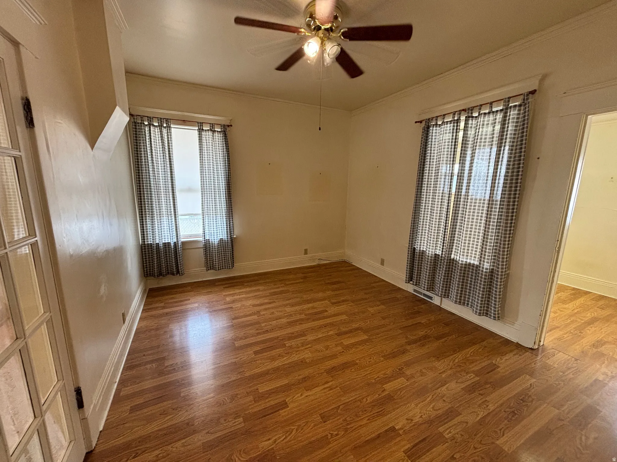 Empty room with wood finished floors, ceiling fan, and ornamental molding