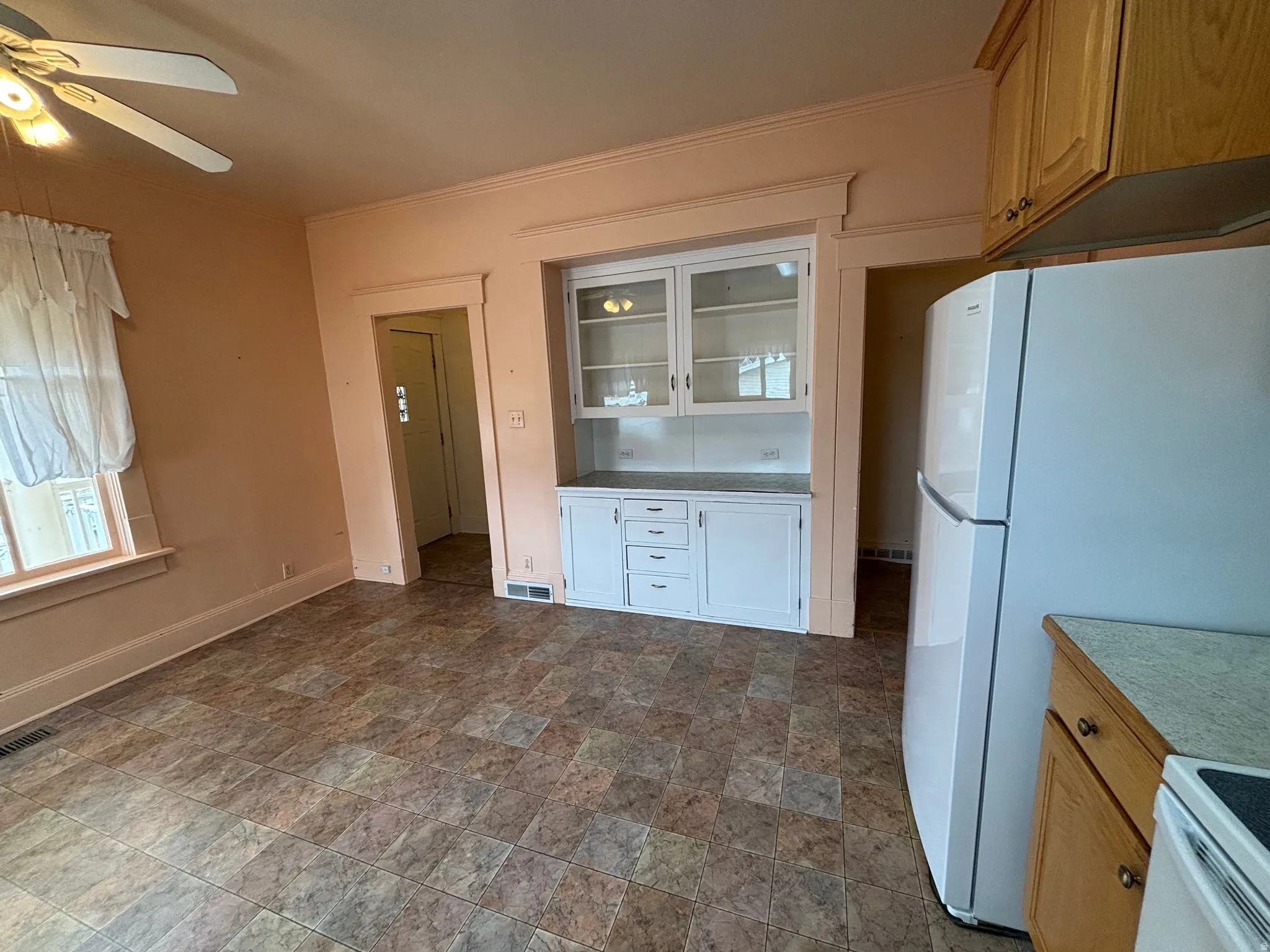 Kitchen with stone finish flooring, white appliances, glass insert cabinets, light countertops, and ornamental molding