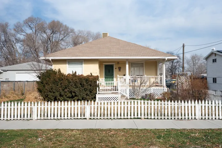 View of front of home with a porch, a chimney, a shingled roof, a fenced front yard, and a garage
