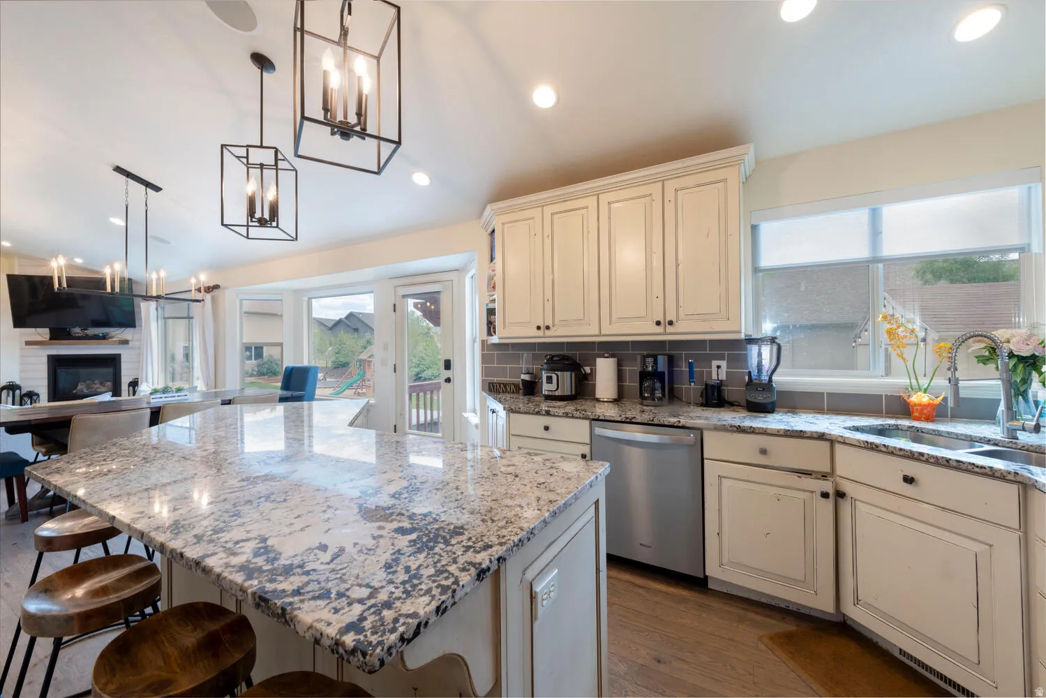 Kitchen featuring cream cabinets, open floor plan, dark wood-type flooring, light stone countertops, and a glass covered fireplace