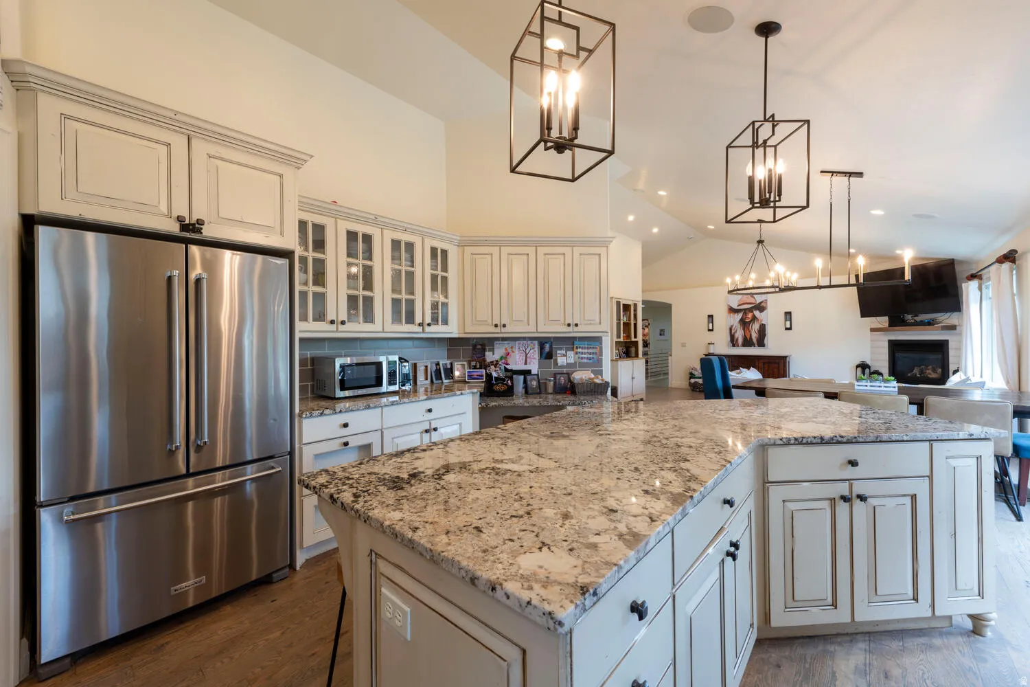 Kitchen with appliances with stainless steel finishes, lofted ceiling, glass insert cabinets, light stone countertops, and open floor plan
