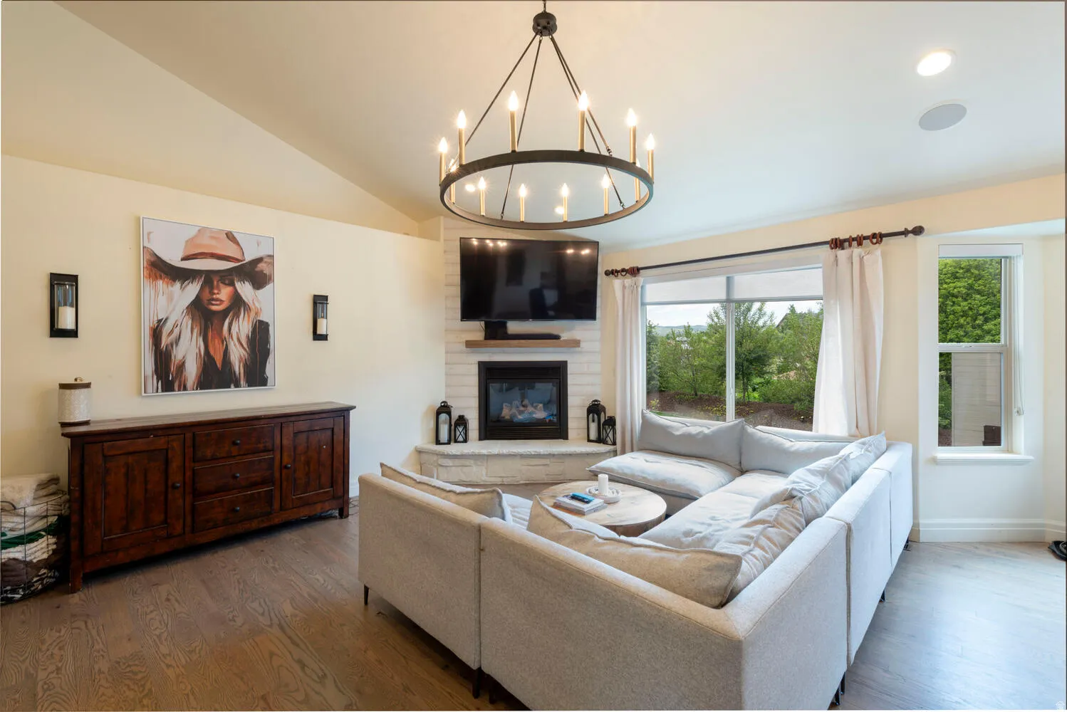 Living area featuring vaulted ceiling, wood finished floors, a large fireplace, and a chandelier