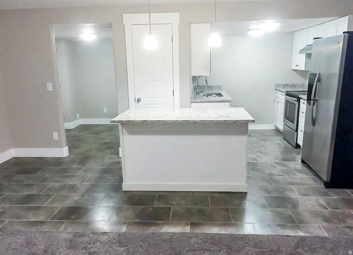 Kitchen featuring white cabinetry, stainless steel appliances, hanging light fixtures, a kitchen island, and under cabinet range hood