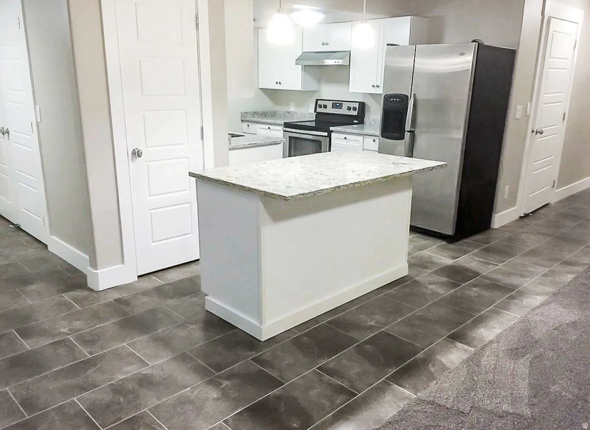 Kitchen with stainless steel appliances, white cabinets, a kitchen island, decorative light fixtures, and range hood