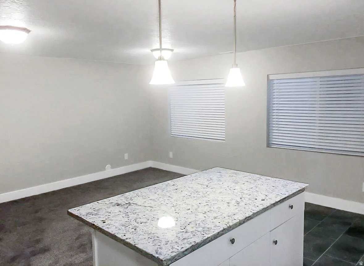 Kitchen with pendant lighting, a kitchen island, light stone counters, and white cabinets