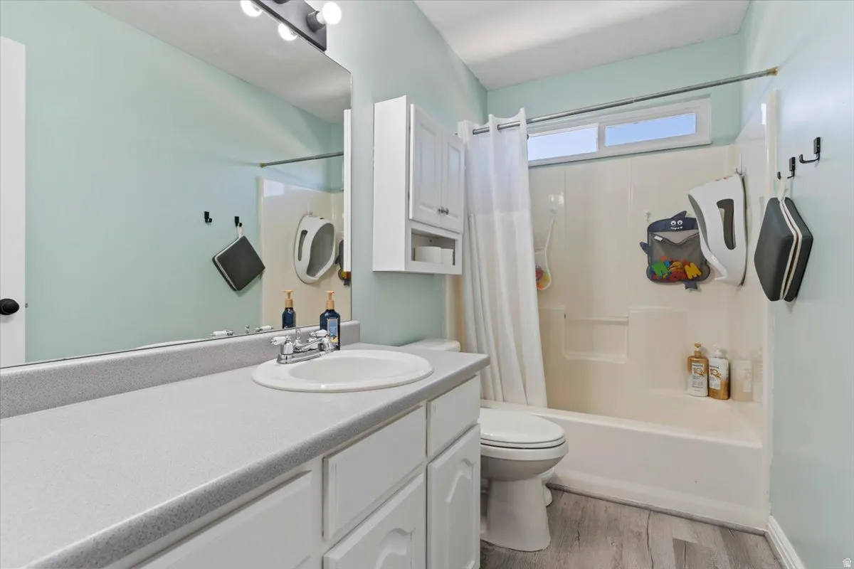 Full bath featuring vanity, shower / bathtub combination with curtain, and light wood-type flooring