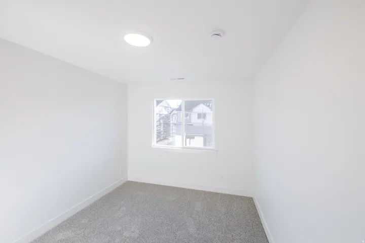 Bright interior room featuring a window with white trim, gray carpet flooring, and a flush-mount ceiling light