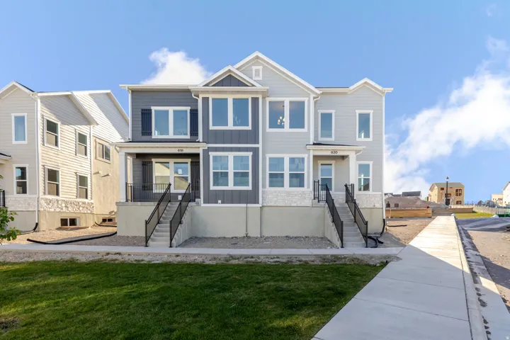 Contemporary townhome exterior featuring multi-toned siding, stone accents, multiple large windows, and a black metal railing on the front steps