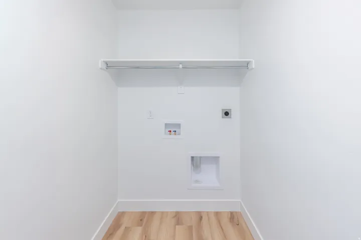Dedicated laundry space featuring a white shelf with a hanging rod, modern utility hookups, and wood-finish flooring