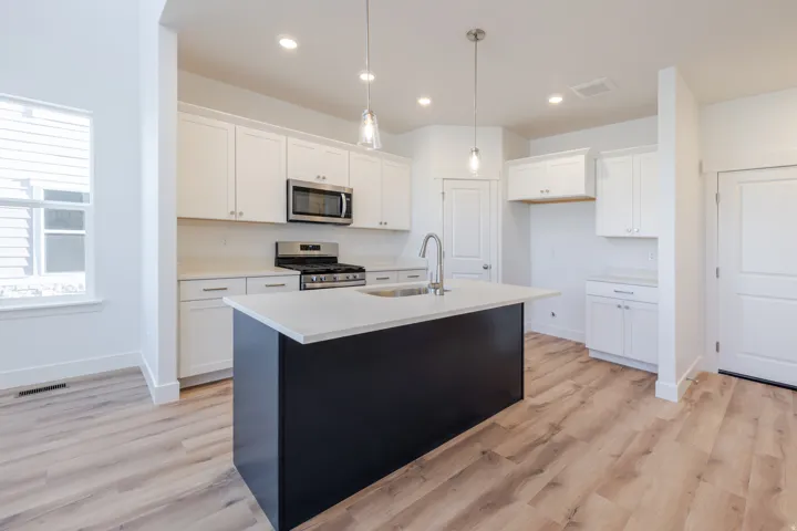 Modern kitchen featuring white cabinetry, stainless steel appliances, a center island with a dark base, and wood-finish flooring