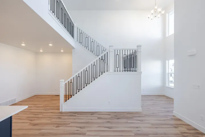 Two-story entrance featuring a white staircase with black metal balusters, wood-finish flooring, recessed lighting, and a modern chandelier