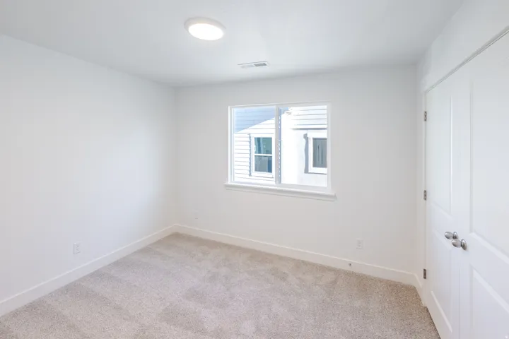 Bright interior room featuring a window with white trim, light gray carpeting, and white walls