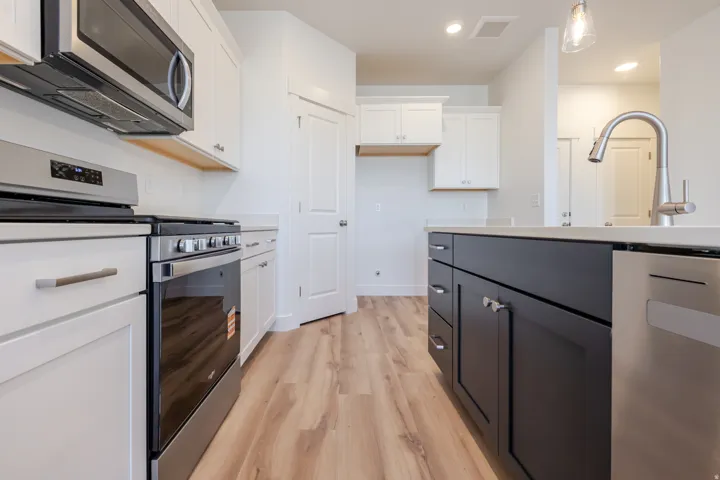 Modern kitchen featuring stainless steel appliances, two-tone cabinetry, quartz countertops, and wood-finish flooring
