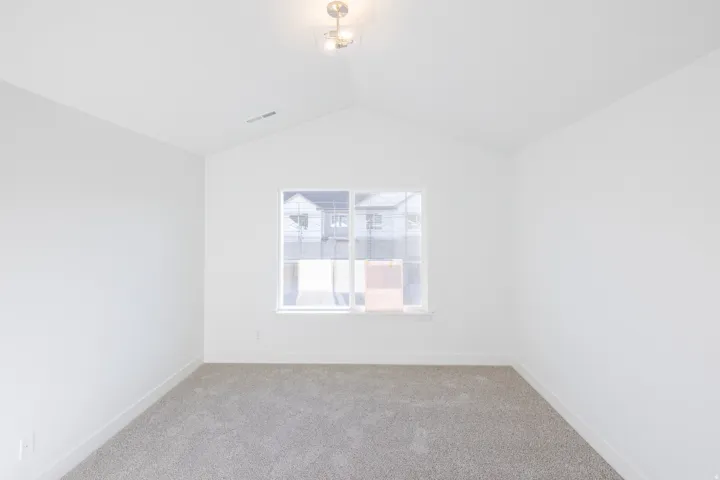 White walls with a vaulted ceiling, light gray carpeting, and a double-pane window