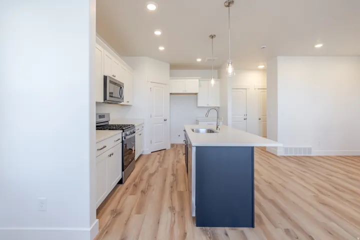 Open-concept kitchen featuring a central island with a sink, white cabinetry, stainless steel appliances, and recessed lighting