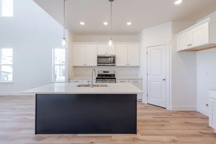 Open-concept kitchen featuring a spacious island with a single-basin sink, white cabinetry, stainless steel appliances, and wood-finish flooring
