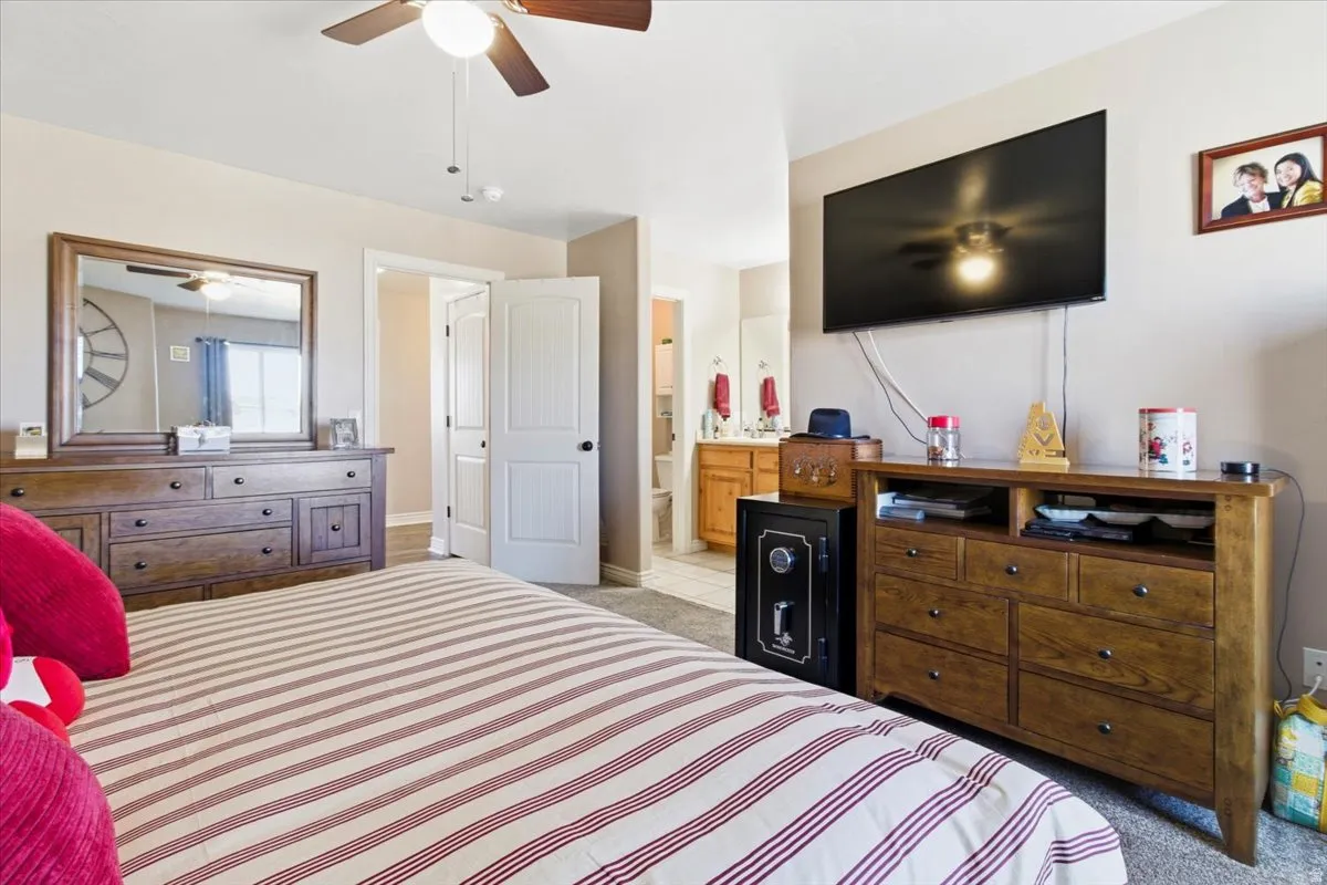 Bedroom with light colored carpet, ensuite bath, and a ceiling fan