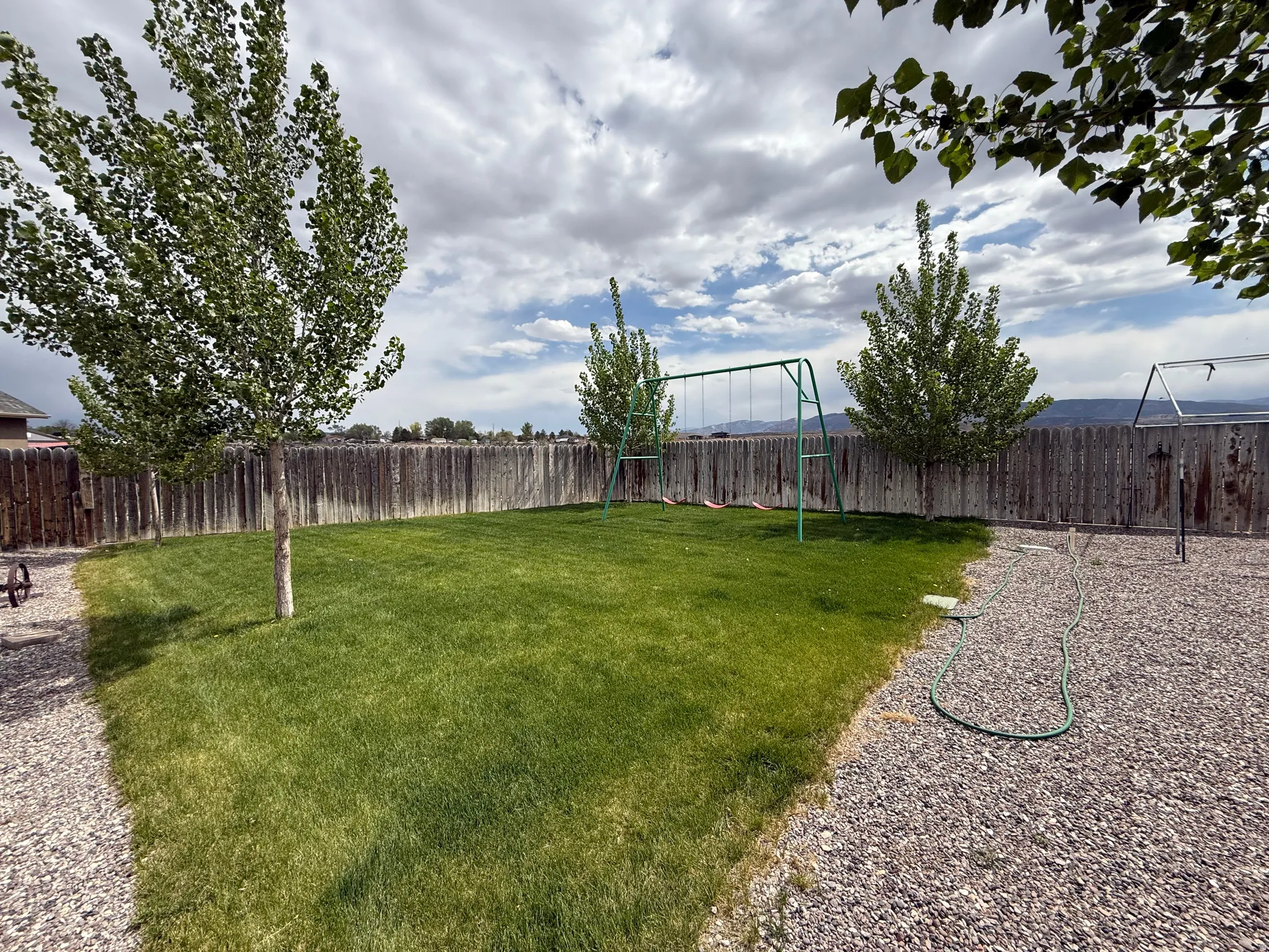 Expansive backyard featuring a lush lawn, mature trees, a wooden privacy fence, and gravel landscaping