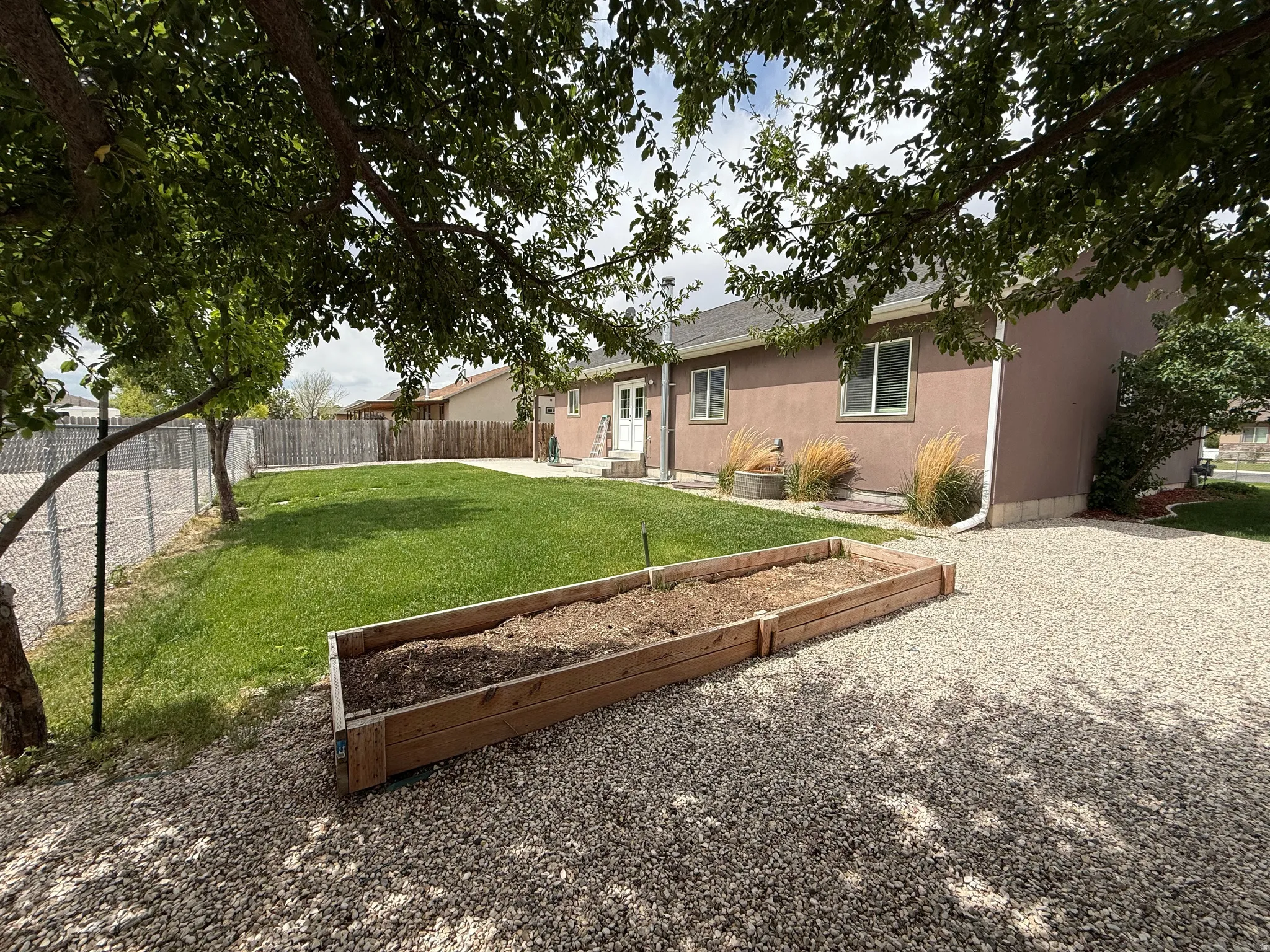 Expansive backyard featuring a gravel patio, raised garden beds, a manicured lawn, and mature trees