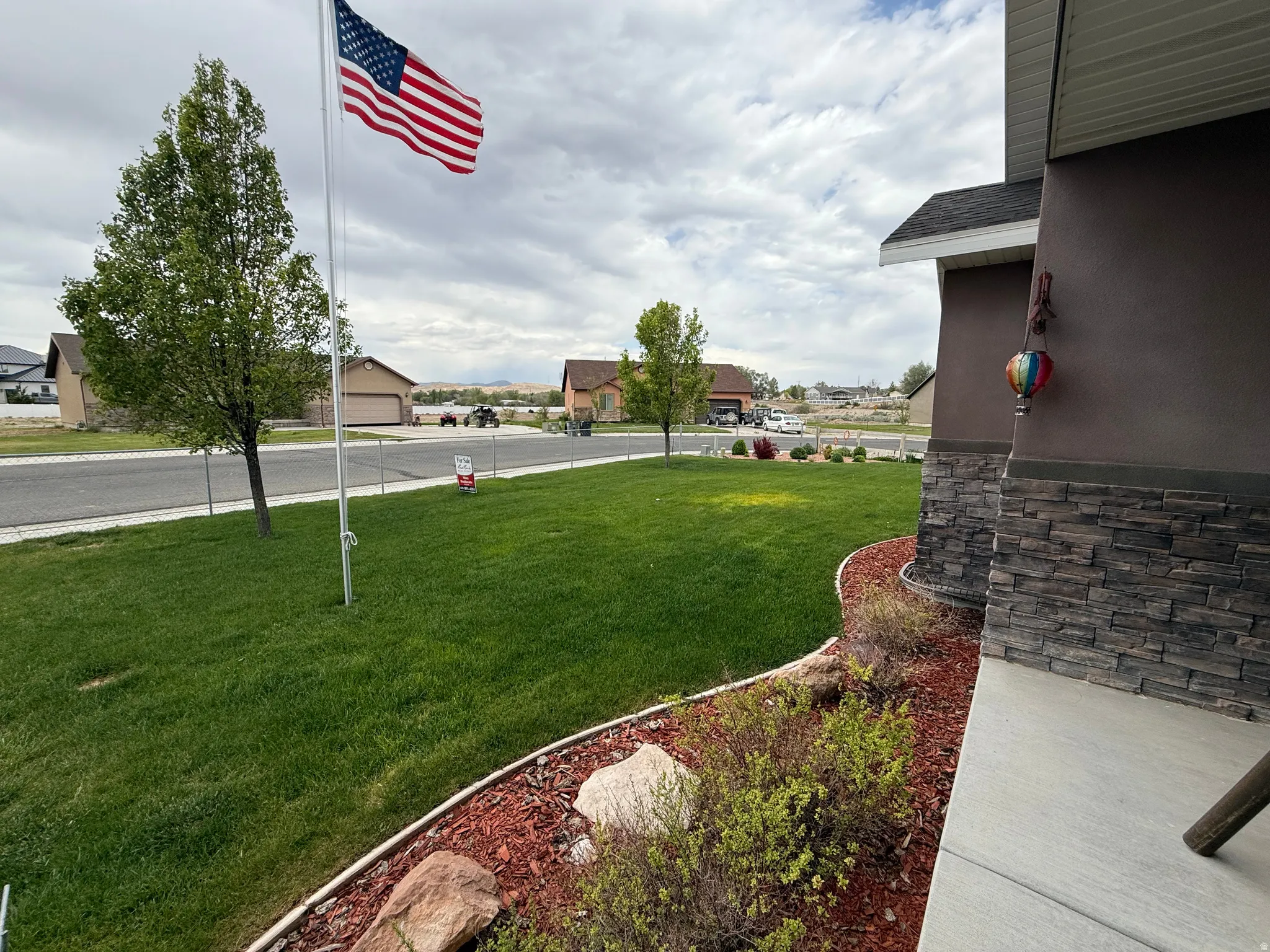 Well-maintained lawn with mature trees, a decorative rock and mulch border, and a stone veneer exterior accent