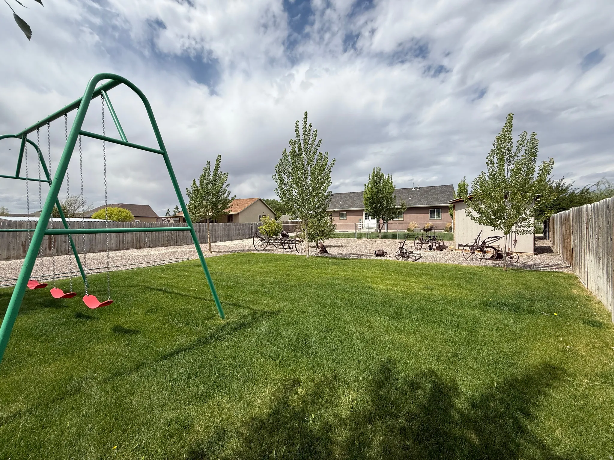 Expansive backyard featuring a lush lawn, gravel perimeter, mature trees, and a storage shed