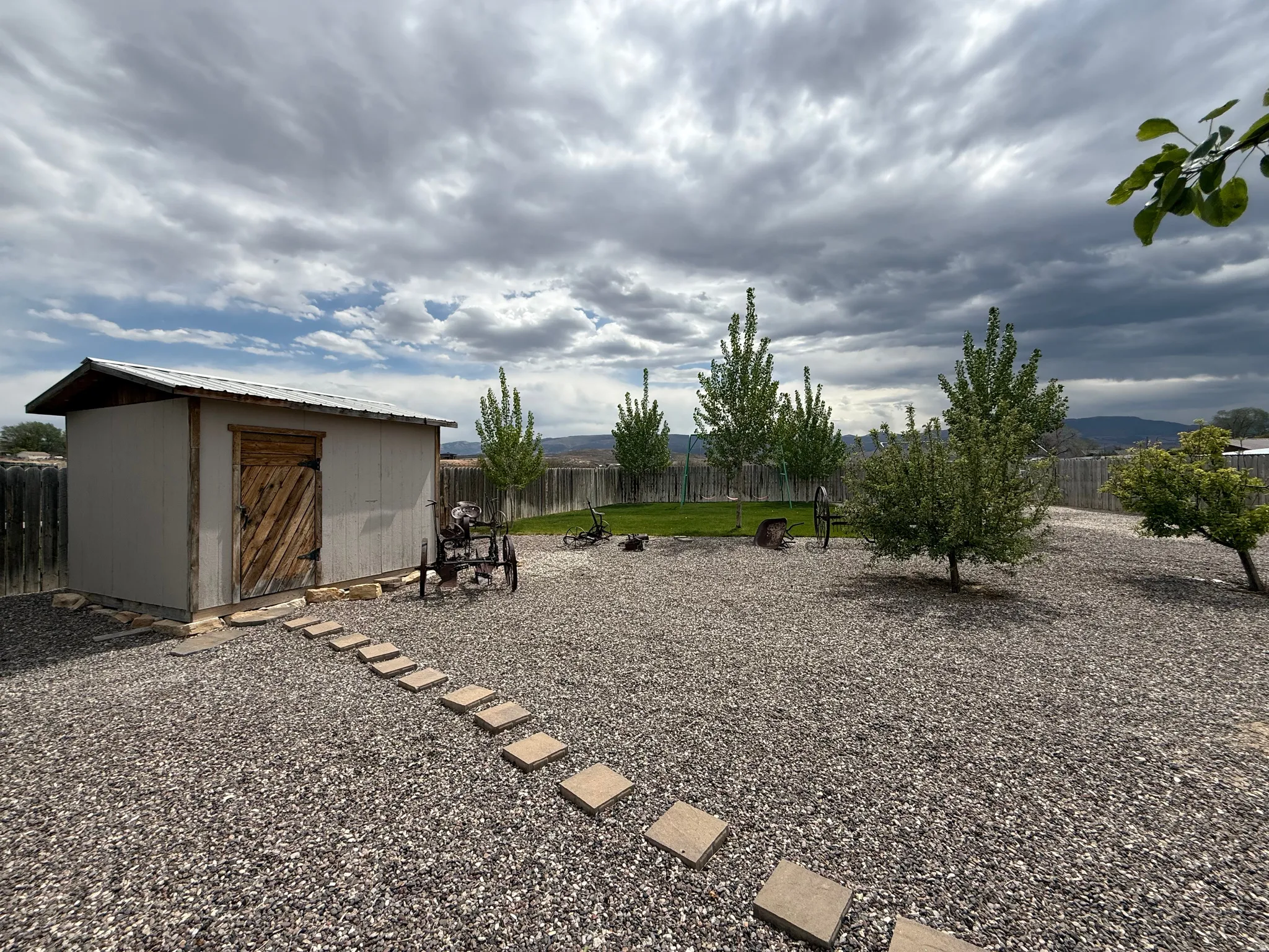 Spacious outdoor area featuring a storage shed with a wood door, gravel ground cover, a stepping stone path, and a wooden perimeter fence