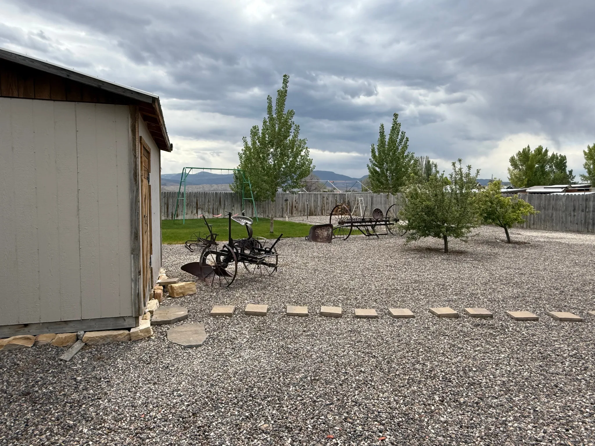 Backyard featuring a gravel surface, a storage shed with wood trim, a wooden privacy fence, mature trees, and a stone paver path