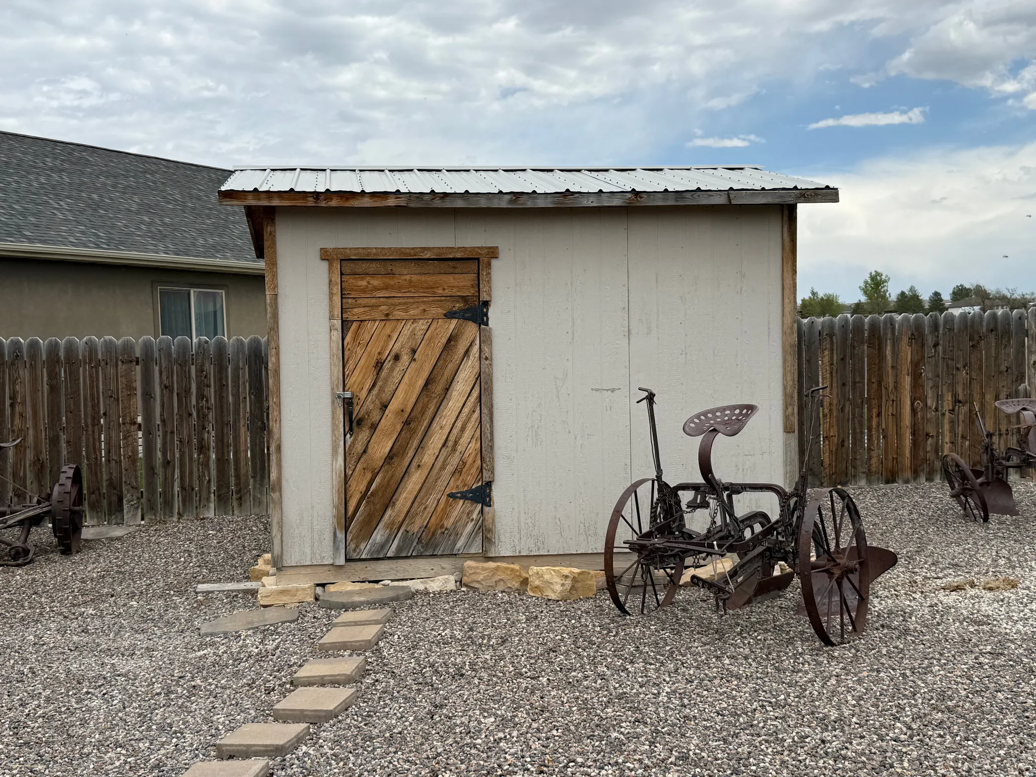 Storage shed with a corrugated metal roof, wooden door, and light-colored siding