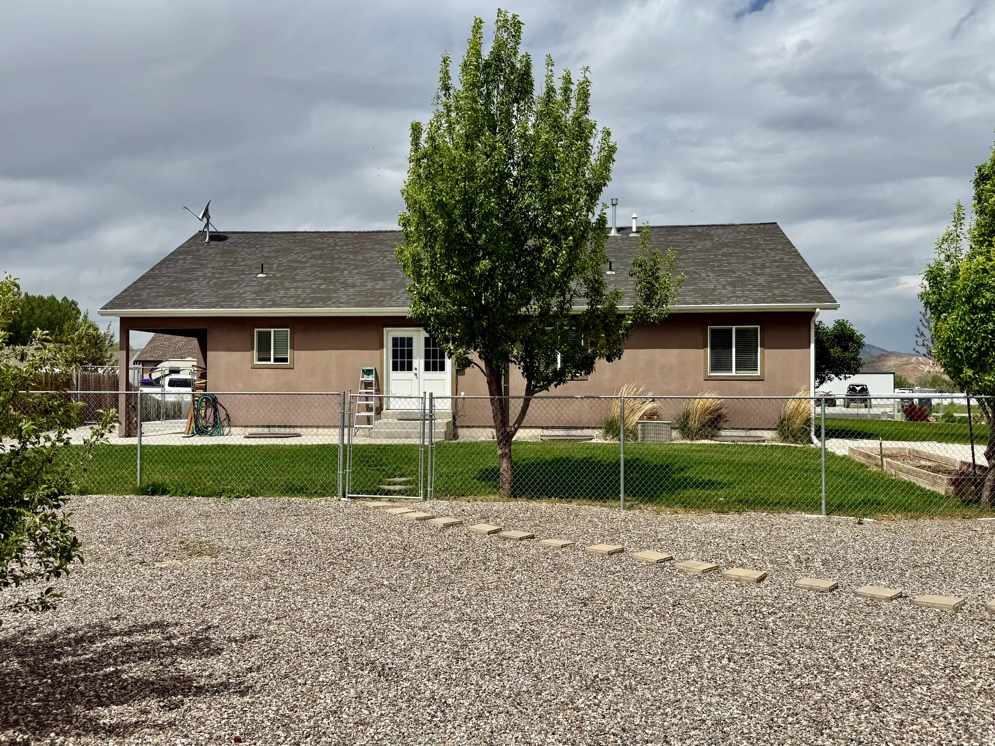 Rear exterior featuring a brown stucco finish, a dark gray shingle roof, and multiple windows
