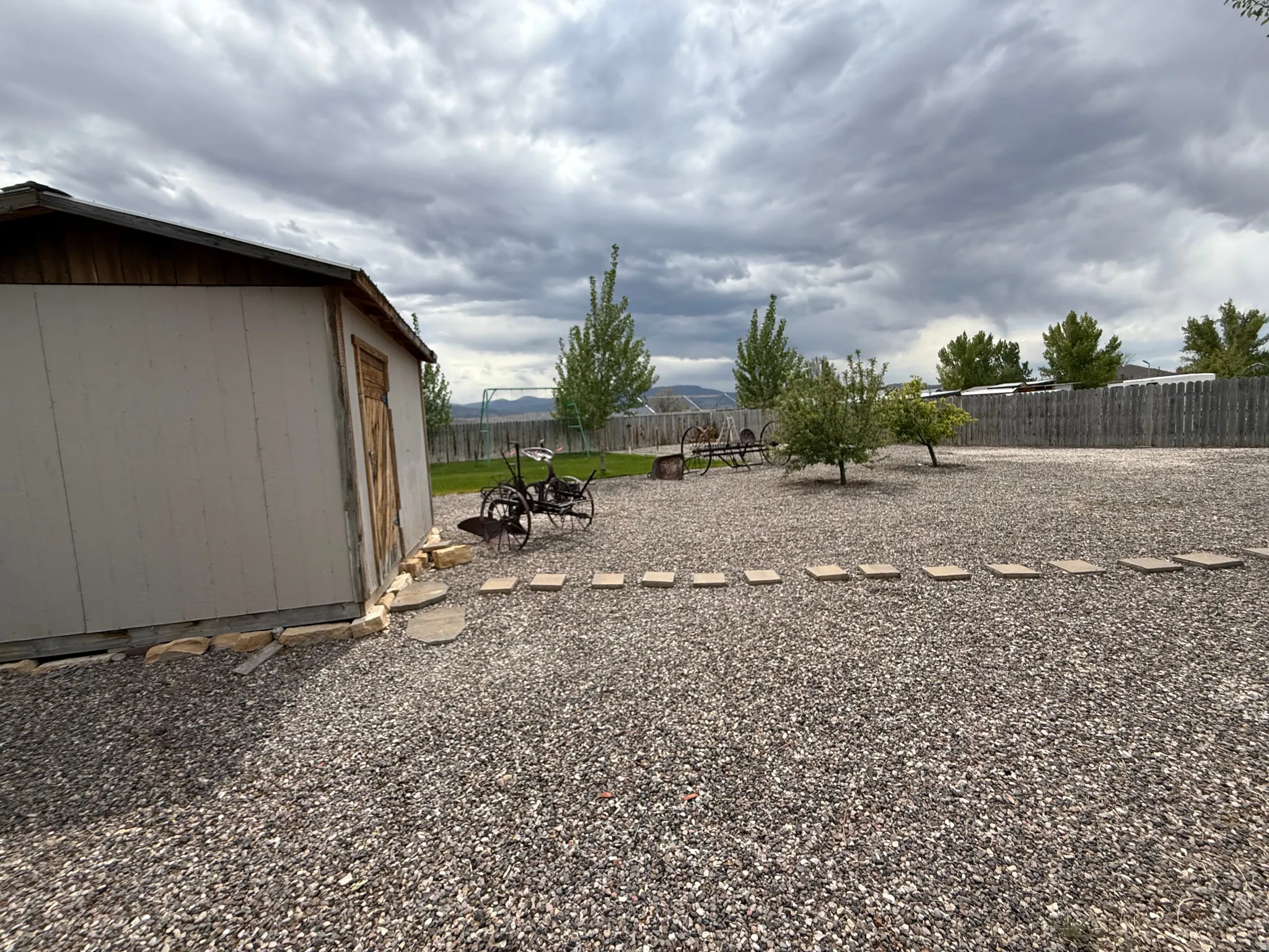 Rear yard featuring extensive gravel surfacing, a wooden storage shed, mature trees, and a perimeter wooden fence