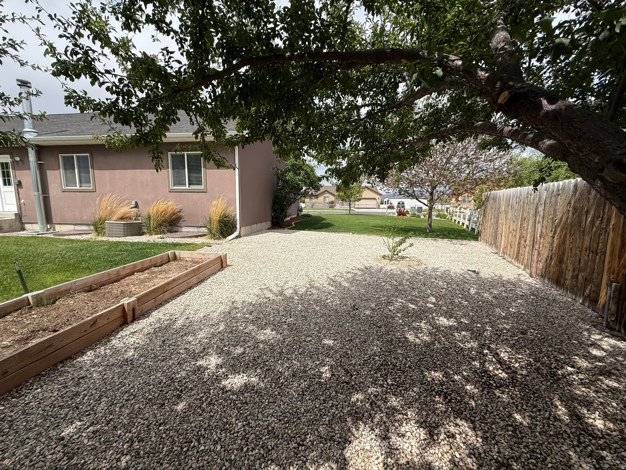 Gravel ground cover in a private backyard featuring a mature shade tree, a wooden privacy fence, and raised garden beds