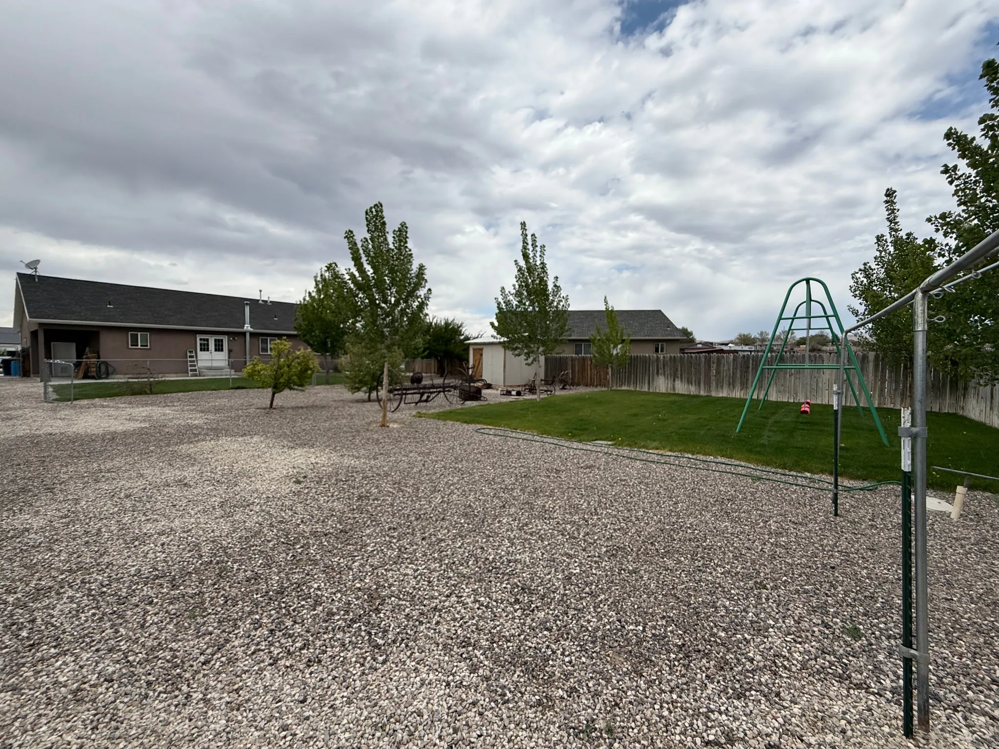 Spacious backyard featuring a large gravel area, a section of manicured lawn, and mature trees