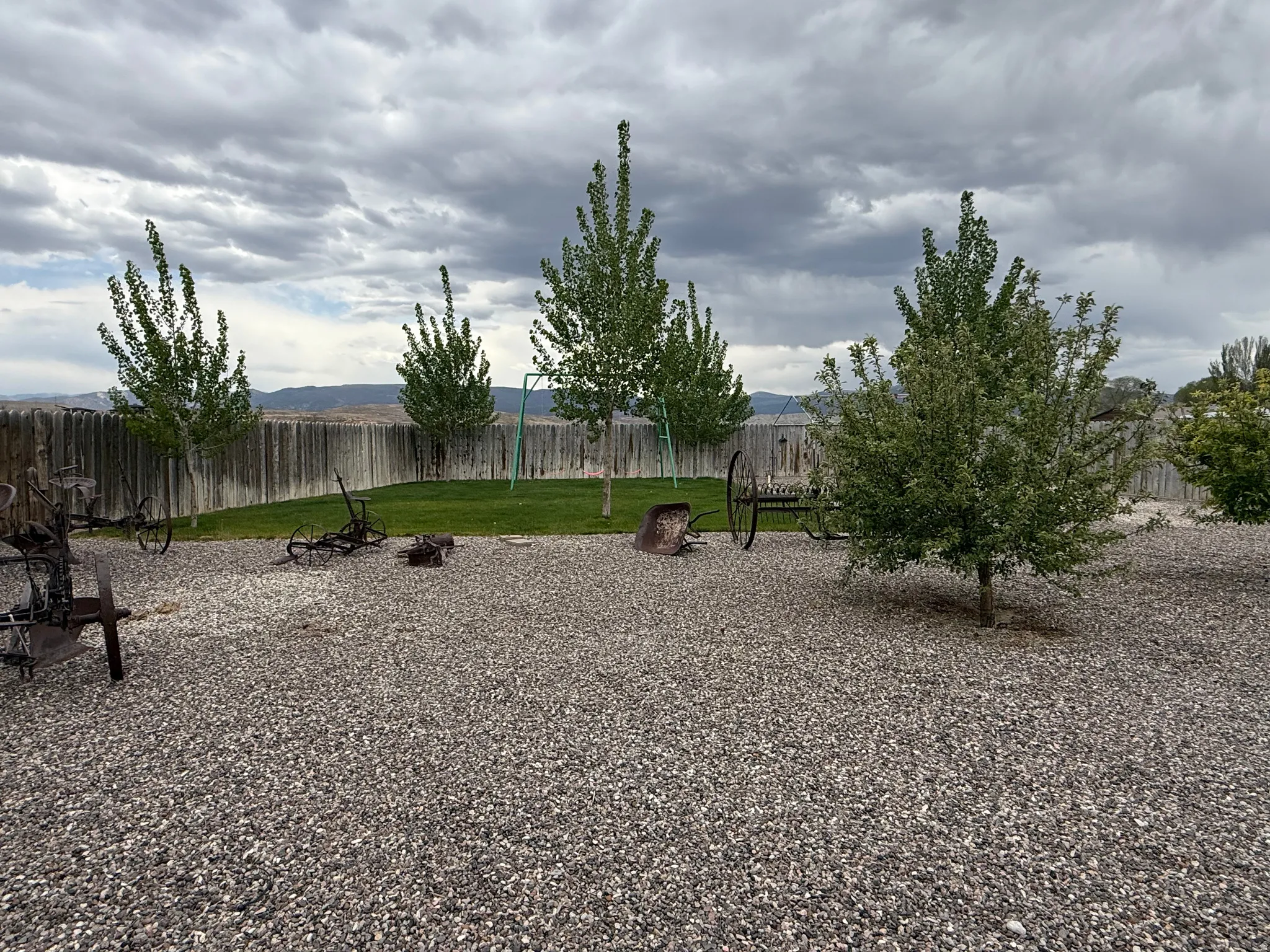 Expansive gravel patio area with mature trees and a fenced perimeter
