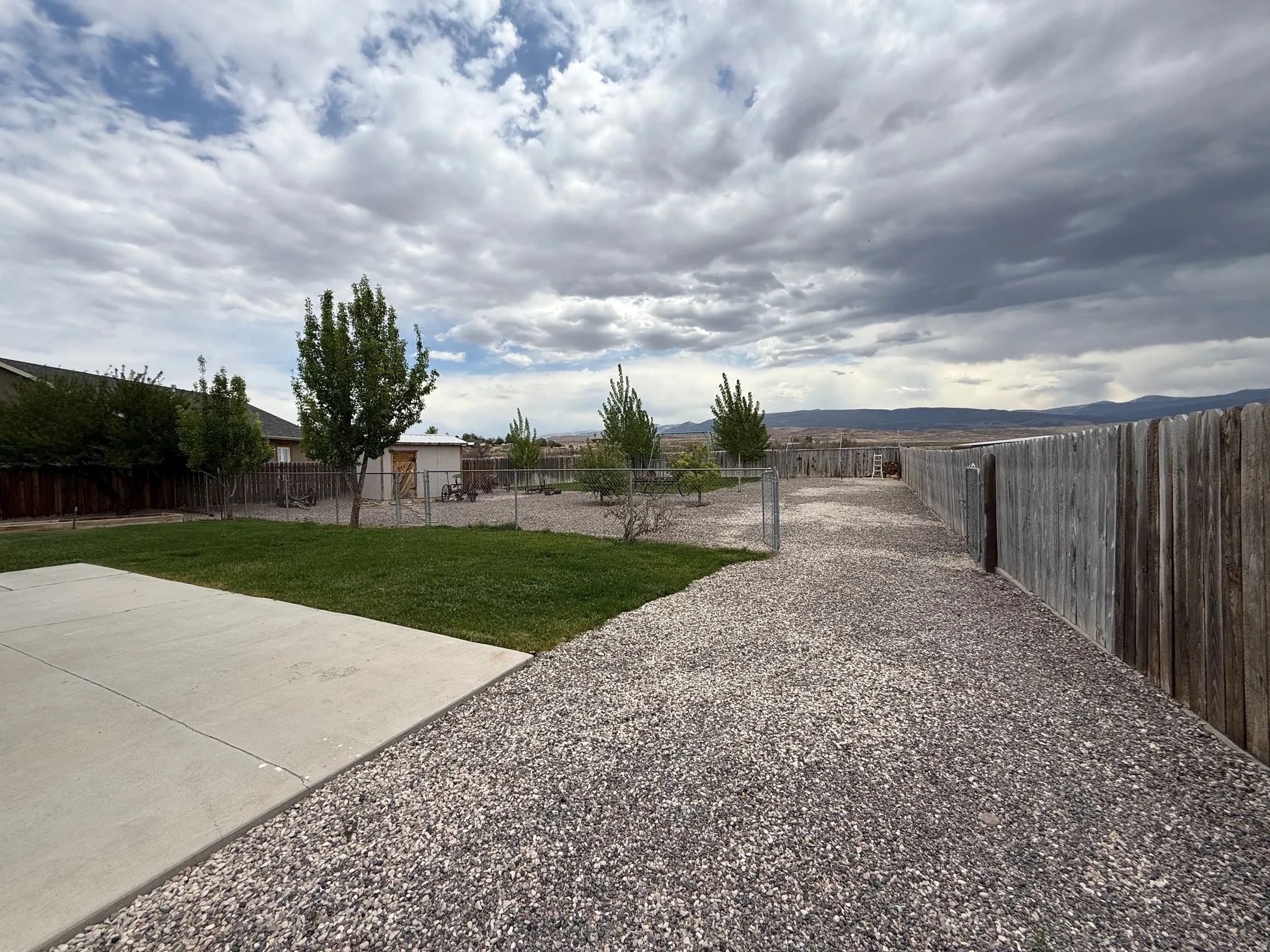 Expansive outdoor space featuring a concrete patio, manicured lawn, gravel pathways, and mature trees