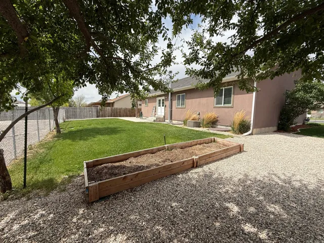 Expansive backyard featuring a gravel patio, raised garden beds, a manicured lawn, and mature trees