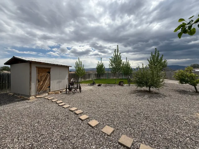 Spacious outdoor area featuring a storage shed with a wood door, gravel ground cover, a stepping stone path, and a wooden perimeter fence