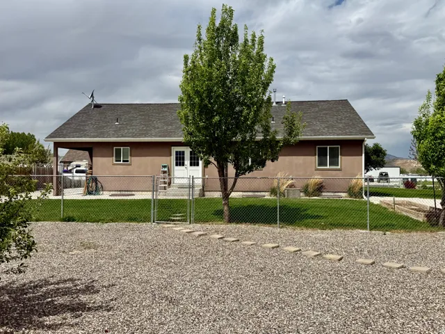 Rear exterior featuring a brown stucco finish, a dark gray shingle roof, and multiple windows