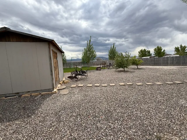 Rear yard featuring extensive gravel surfacing, a wooden storage shed, mature trees, and a perimeter wooden fence