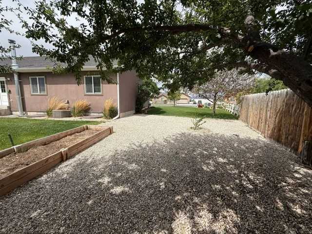 Gravel ground cover in a private backyard featuring a mature shade tree, a wooden privacy fence, and raised garden beds