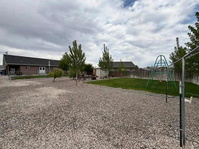 Spacious backyard featuring a large gravel area, a section of manicured lawn, and mature trees