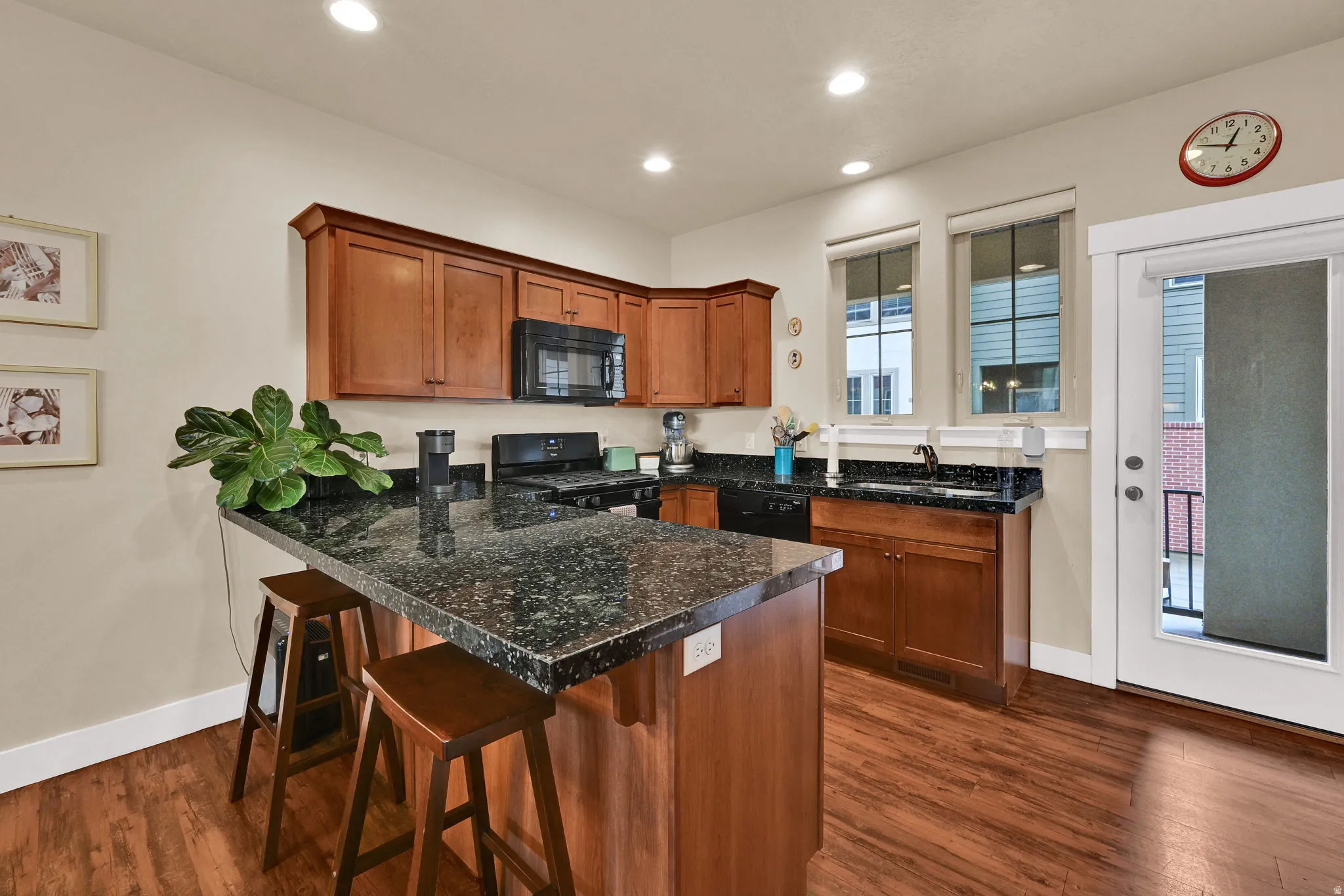 Kitchen with brown cabinets, black appliances, a kitchen breakfast bar, a peninsula, and dark wood-style flooring