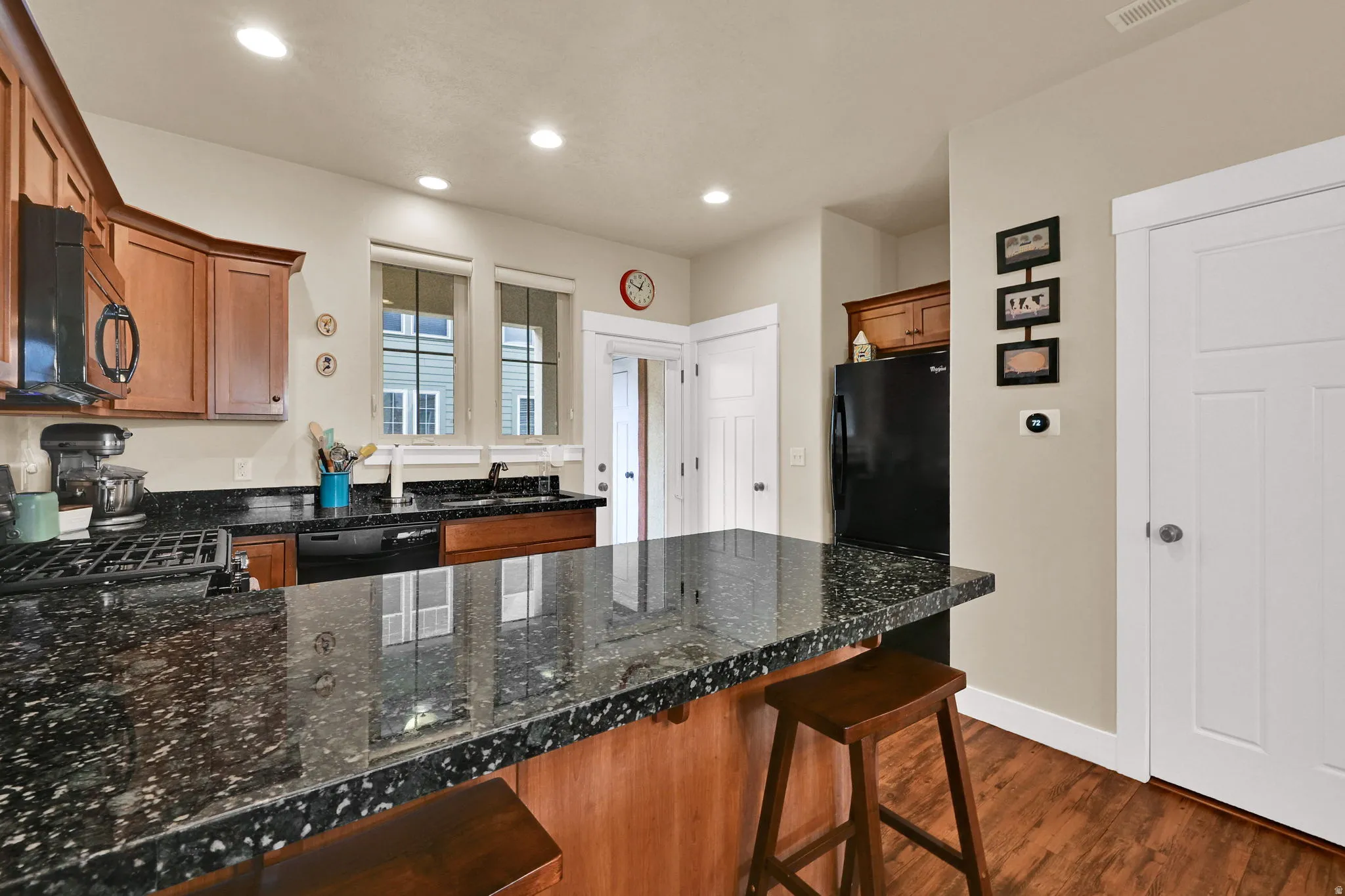 Kitchen with a peninsula, brown cabinets, a kitchen breakfast bar, black appliances, and dark wood-style floors