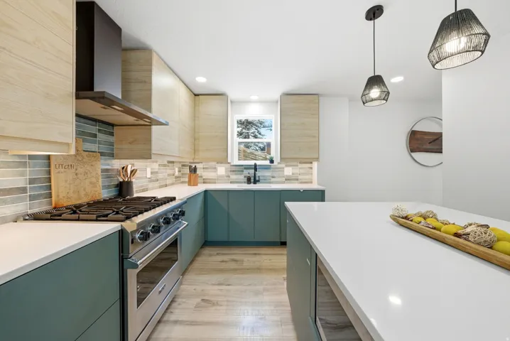 Kitchen with stainless steel stove, wall chimney range hood, pendant lighting, modern cabinets, and green cabinets