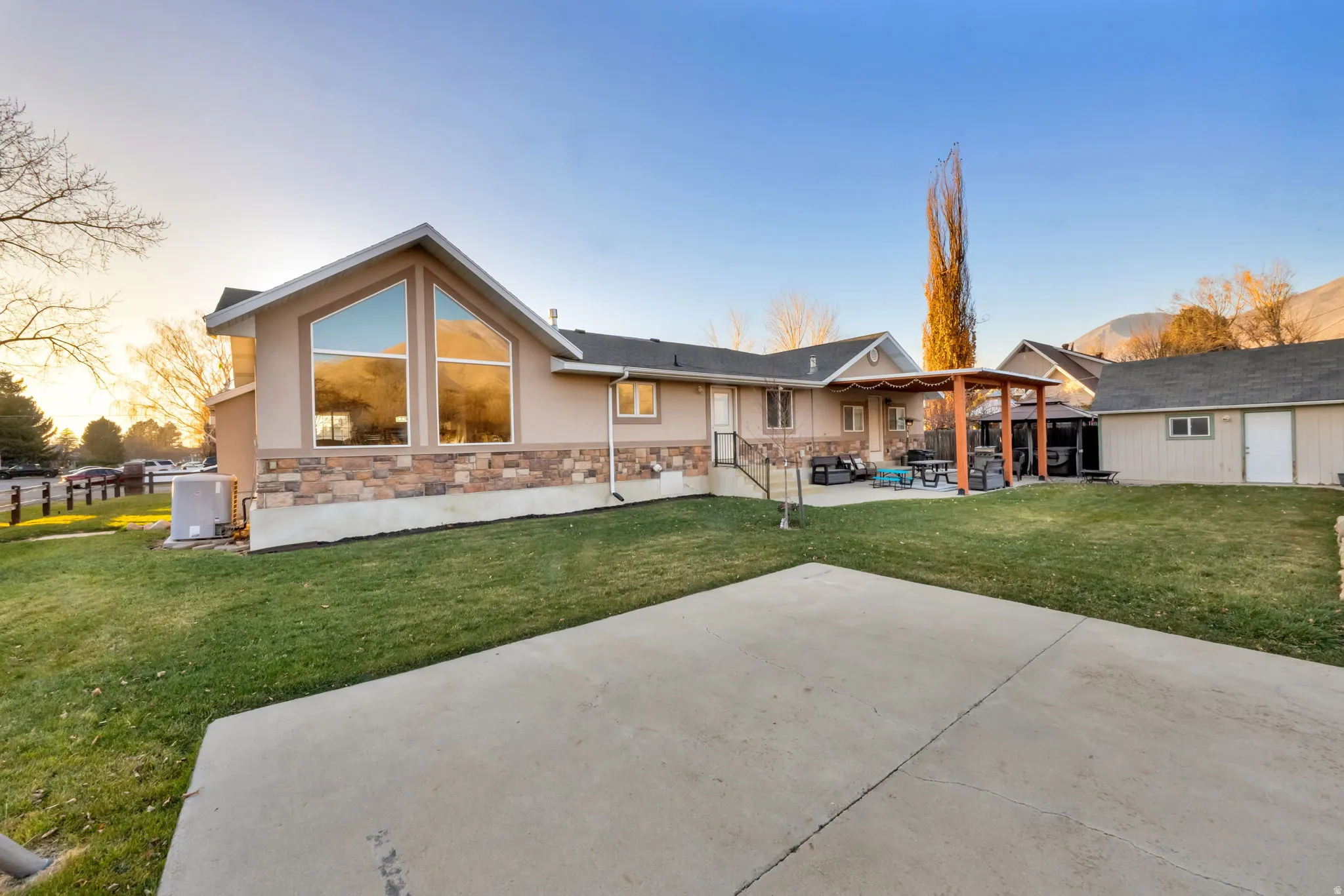 Rear view of property featuring a patio, a yard, stone siding, and stucco siding