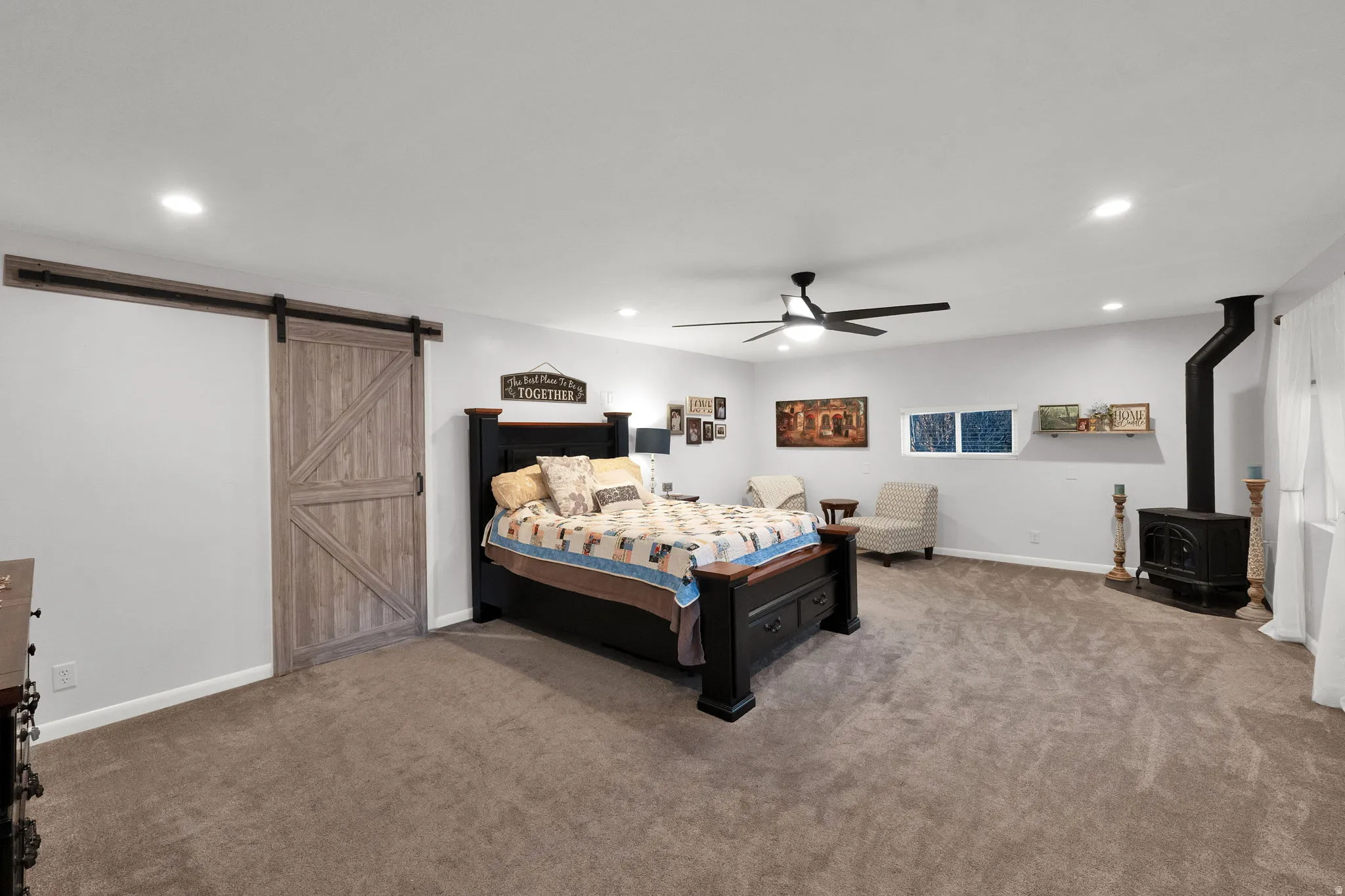 Bedroom with a wood stove, carpet, a barn door, ceiling fan, and recessed lighting